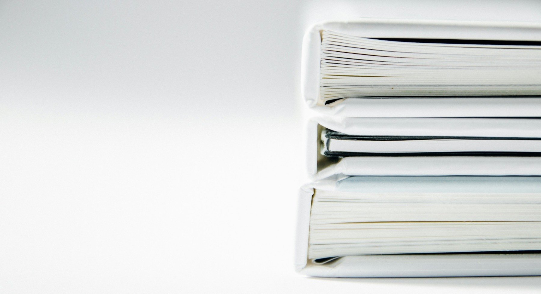 A stack of thick white binders on a white desk